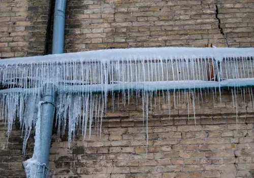 Icicles hanging from a frozen pipe on a brick wall during a hard freeze