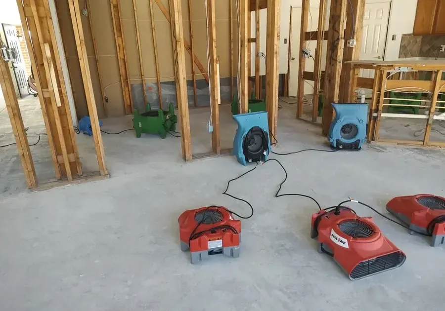 Air movers drying exposed wall studs and a bare concrete floor